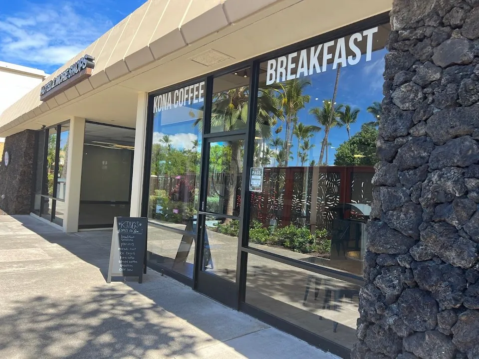 Storefront with KONA COFFEE and BREAKFAST window lettering, a sidewalk chalkboard, and a lava-rock wall.