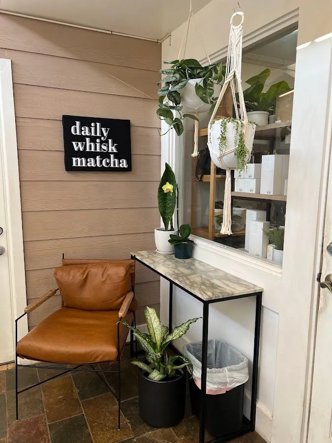 Brown leather chair beside a marble console, hanging plants, and a black wall sign reading daily whisk matcha.