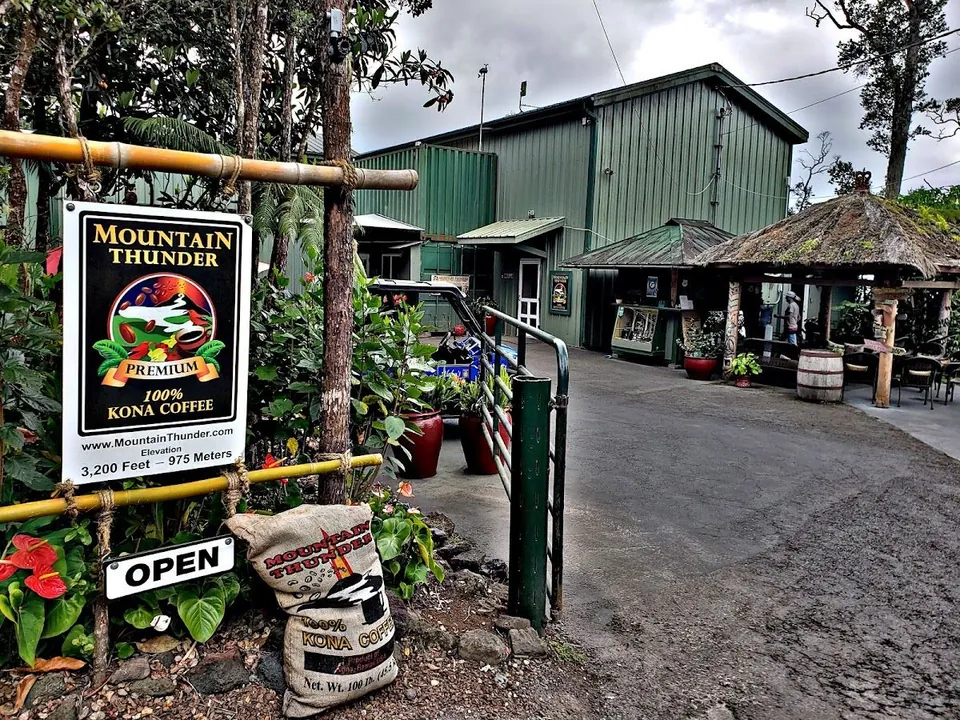Mountain Thunder Kona coffee sign and sack at the entrance of a green building with a thatched pavilion.