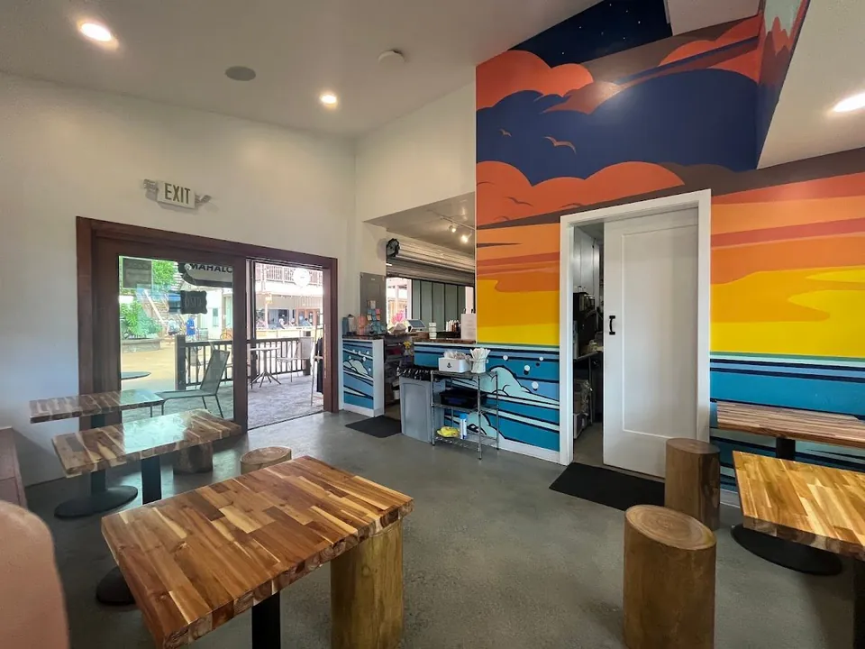 Shop interior with wood tables, log stools, a painted sunset mural, and an open exit door.