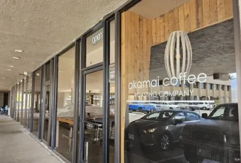 Glass storefront of Akamai Coffee Roasting Company under a covered walkway, with an open sign in the window.