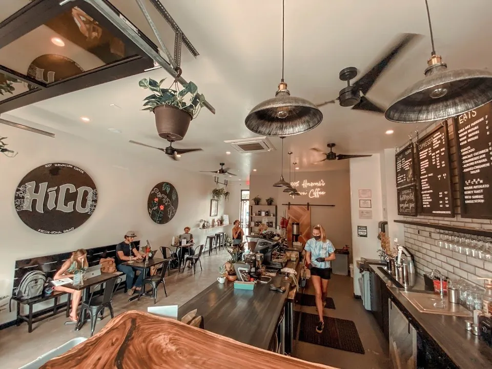 Cafe interior with a round HiCO sign, pendant lamps, a service counter, and people seated at tables.