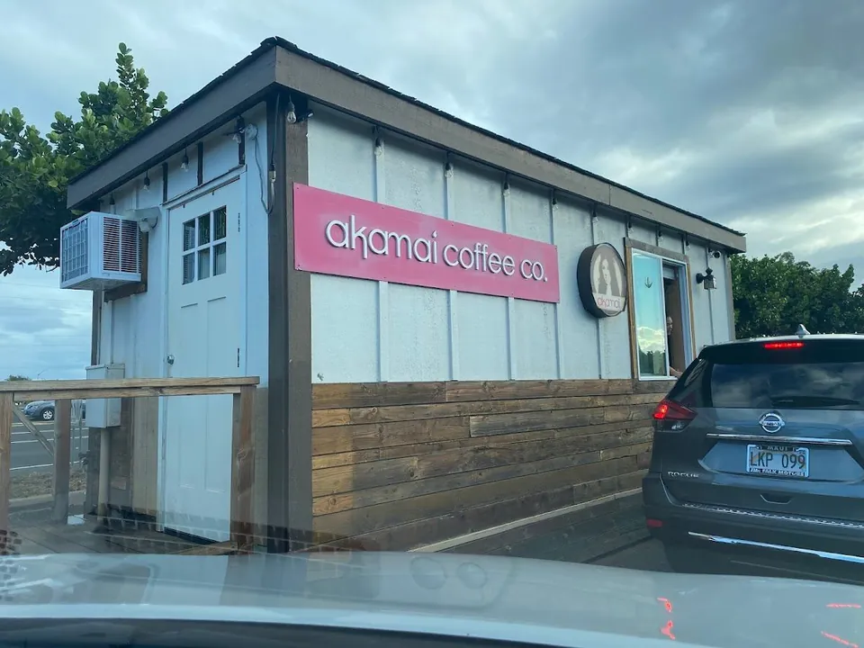 White coffee stand exterior with a pink akamai coffee co. sign and a person at the service window.