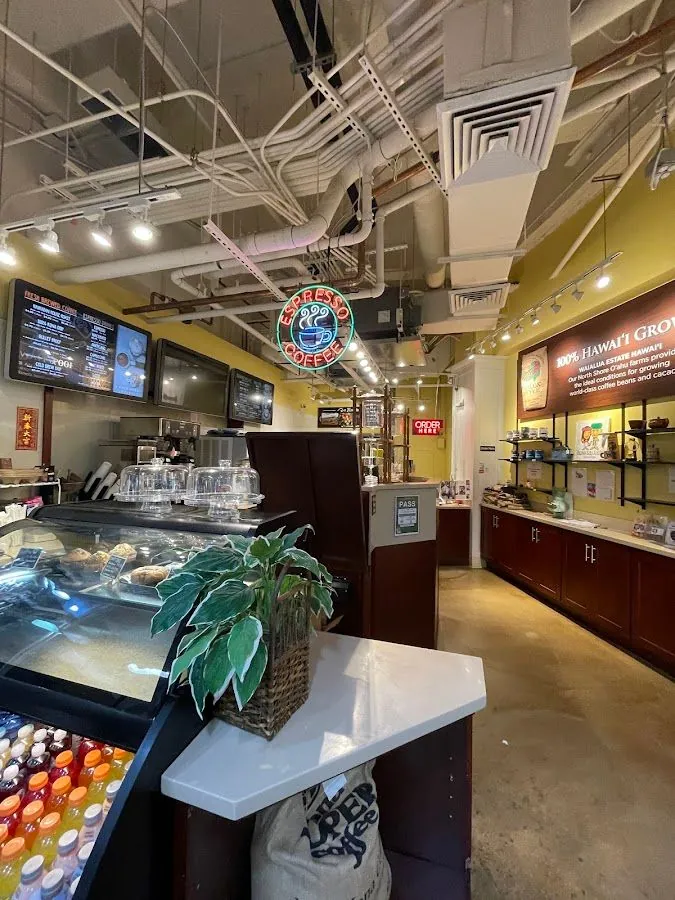 Coffee shop interior with a baked-goods case, menu screens, an espresso neon sign, and a Waialua Estate banner.