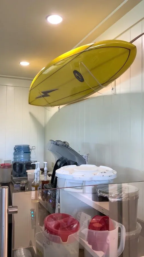 Yellow surfboard hangs above a counter with a water jug, pump bottles, bins, and lidded containers.