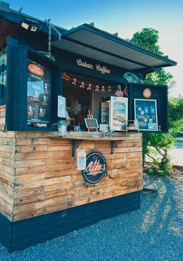 Outdoor wooden coffee kiosk with open shutters, Cuban Coffee lettering, and an Alba's Cuban Coladas sign.