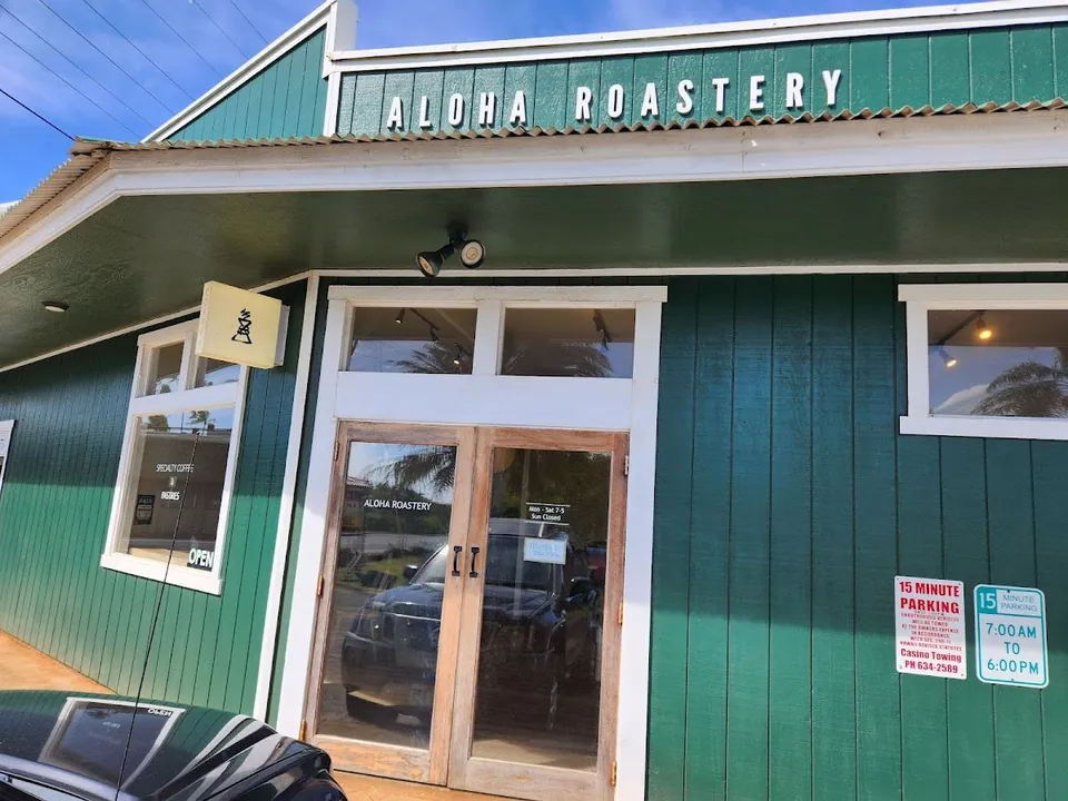 Green wood storefront of Aloha Roastery with the name on the facade, a glass double door, windows, and 15-minute parking signs.