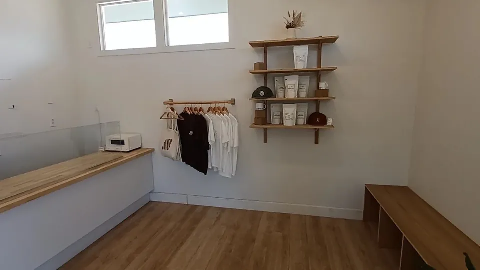 Bright shop interior with a wood counter, hanging shirts and totes, shelves of coffee bags and hats, and a wood bench.