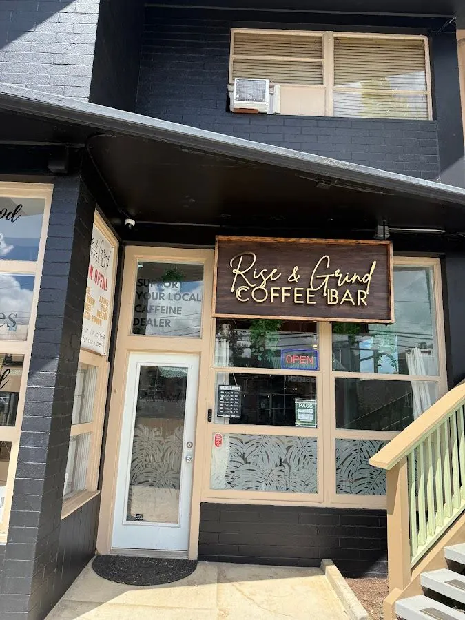 Black-brick Rise & Grind Coffee Bar entrance with a wood sign, glass door, and leaf-etched windows.