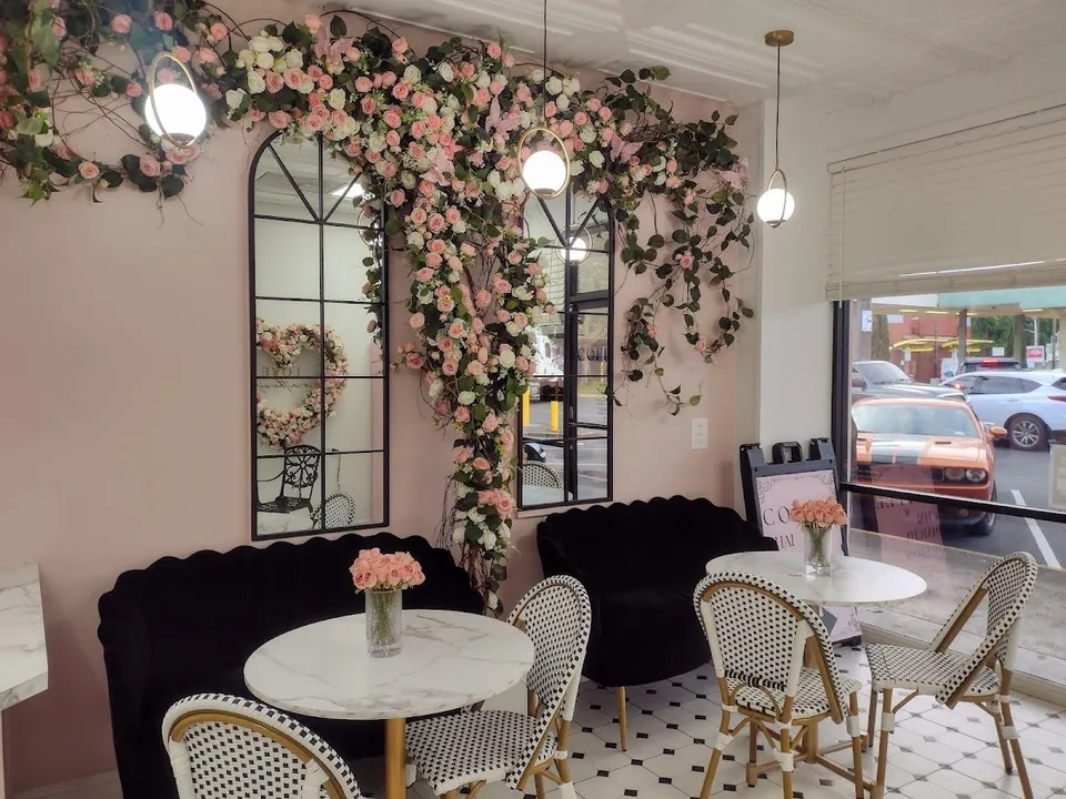 Blush-walled seating area with rose garlands, black scalloped sofas, marble tables, and checkered chairs.