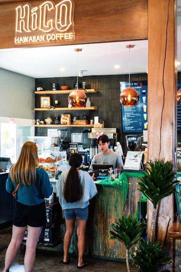 Inside HiCO Hawaiian Coffee, two people stand at the counter while a staff member works the register.