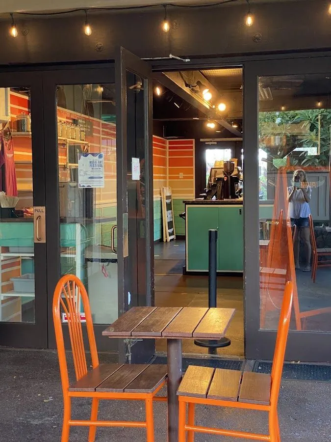 Orange chairs and a wood table sit outside an open glass door under string lights.