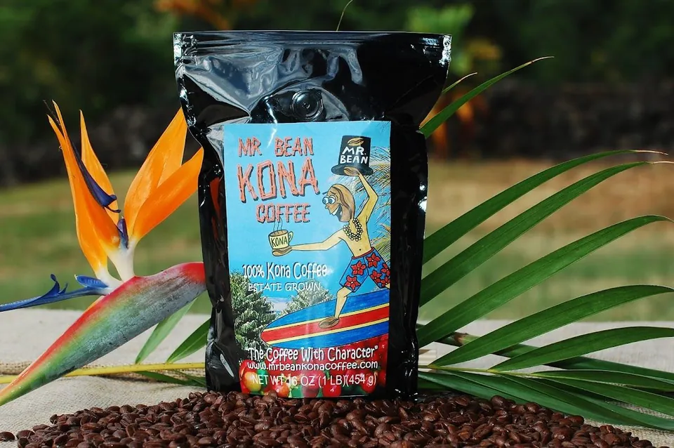 Black Mr. Bean Kona Coffee bag with roasted beans, a bird of paradise flower, and palm leaves.