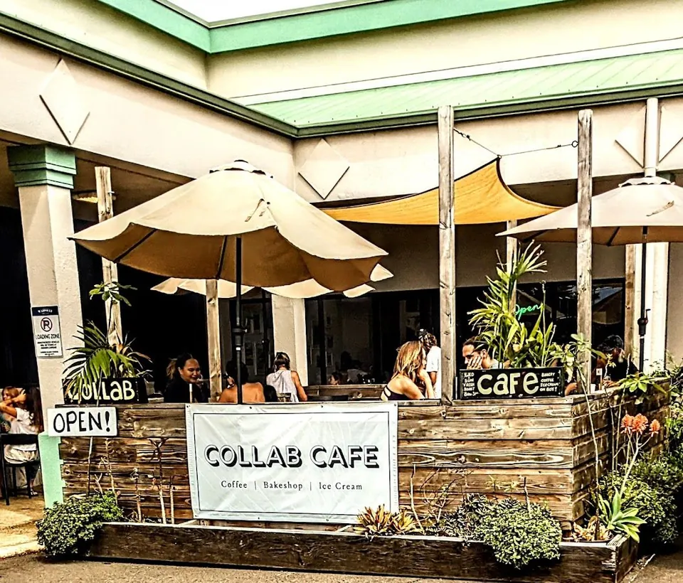 Outdoor patio of Collab Cafe with umbrellas, shade sails, wooden planters, and seated guests.