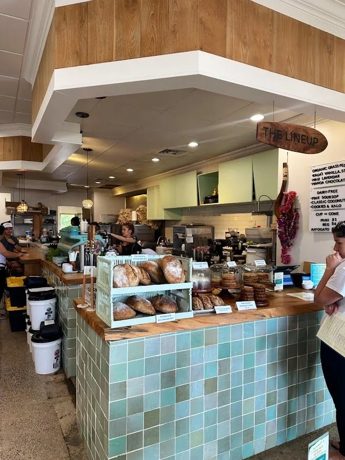 Cafe service counter with bread loaves in crates, a hanging lineup sign, and a wall menu.