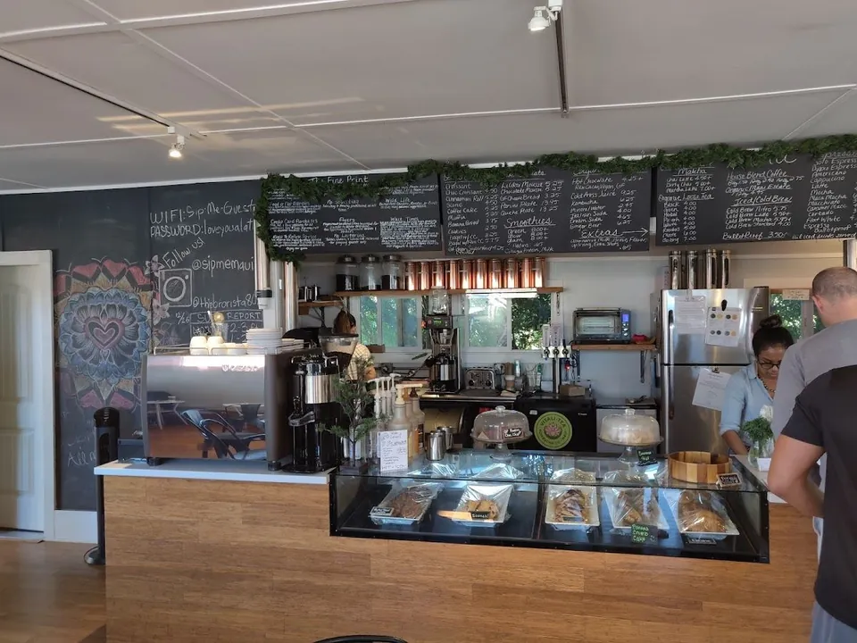 Coffee shop counter with a pastry case, espresso machine, chalkboard menus, and people working.