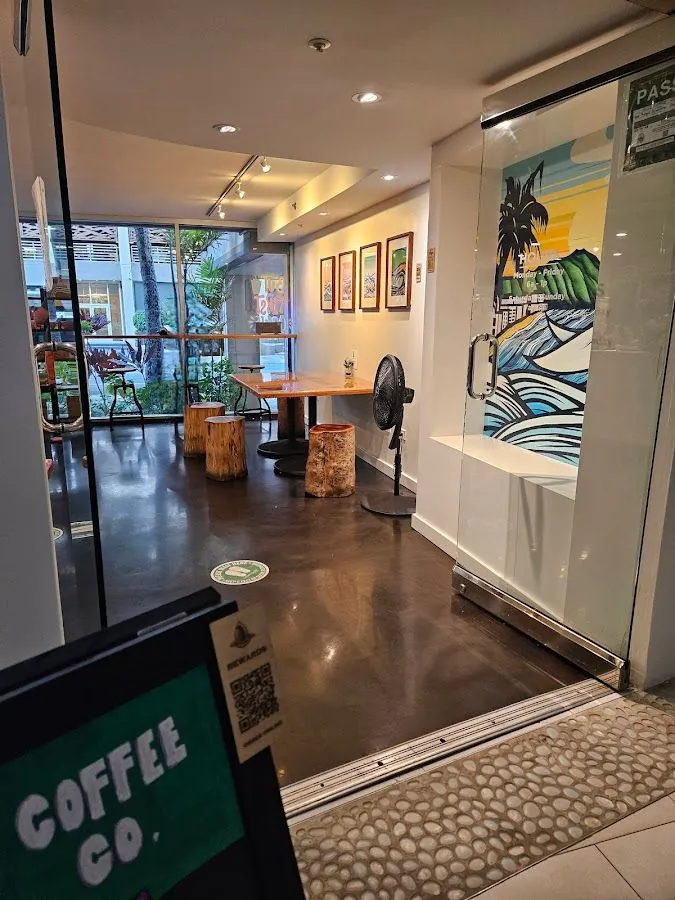 Doorway view into a coffee shop with wood-stump seats, a table, a standing fan, and a Coffee Co. sign.