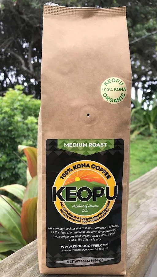 Kraft coffee bag labeled Keopu medium roast 100% Kona organic, standing on a wooden rail outdoors.