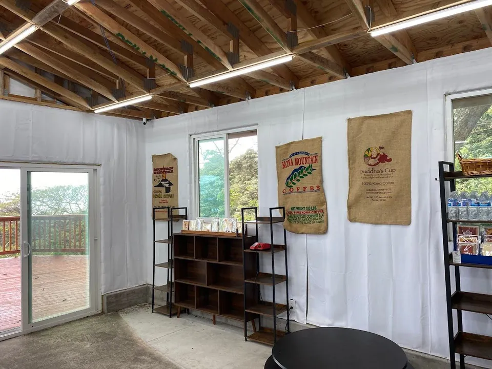 Interior with wood ceiling beams, white walls, black shelves, a round table, and hanging burlap coffee sacks.
