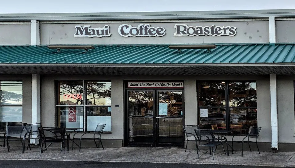 Maui Coffee Roasters storefront with a green awning, outdoor tables, and an open neon sign.