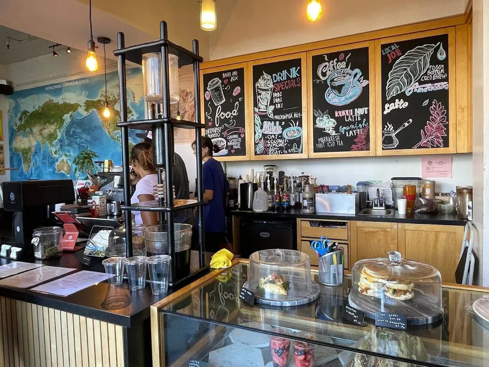 Coffee shop counter with chalkboard drink menus, a pastry case, and staff working behind the bar.