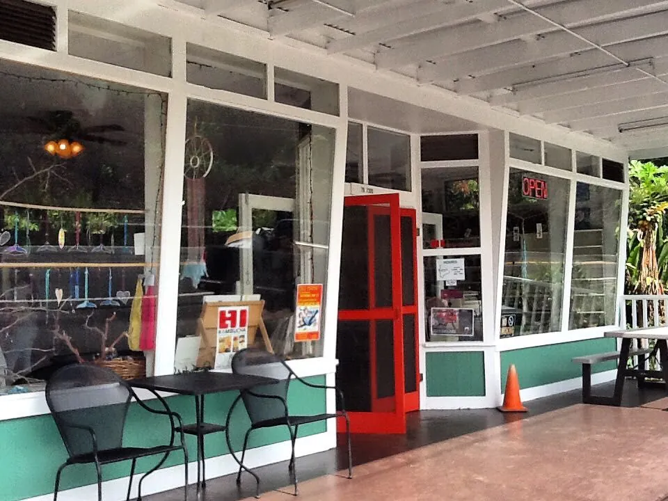 Covered shop porch with teal walls, white trim, a red screen door, metal chairs, and a red OPEN sign.
