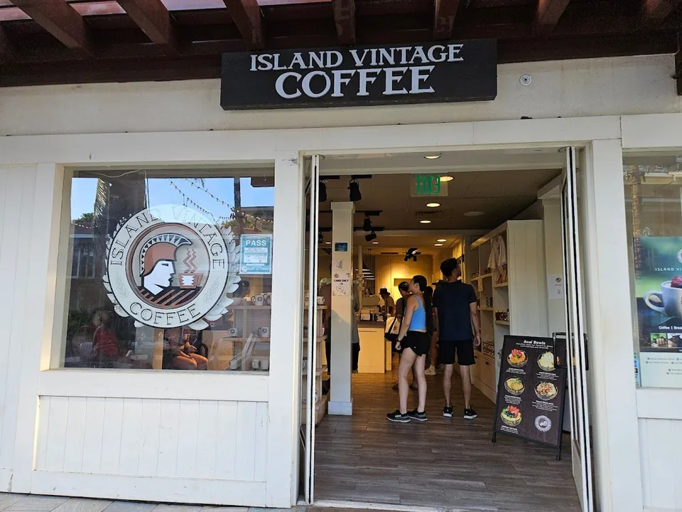 Two people stand in the open Island Vintage Coffee doorway beneath the sign, beside an acai bowls board.