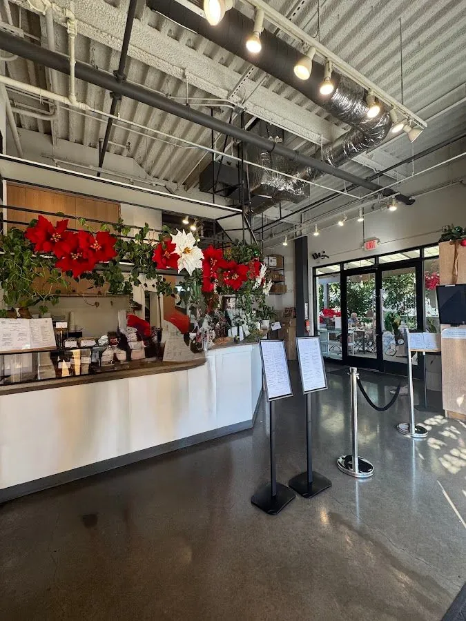 White service counter with red poinsettia garland, menu stands, and glass doors under exposed ceiling ducts.
