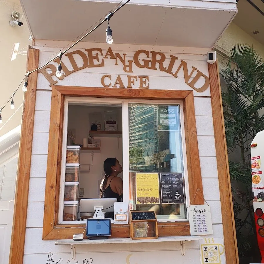 White wooden Ride and Grind Cafe service window with string lights and a person behind the counter.