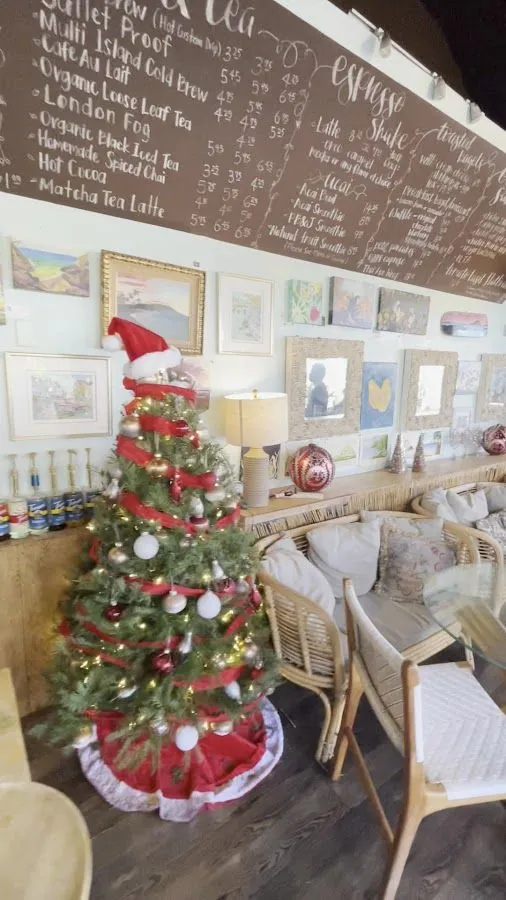 Cafe interior with a decorated Christmas tree, wicker chairs, wall art, and a large handwritten drink menu.
