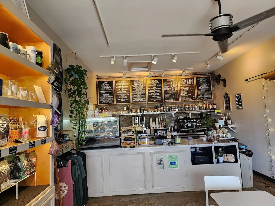 Coffee shop service counter with chalkboard menus, espresso machine, pastry case, and retail shelves.