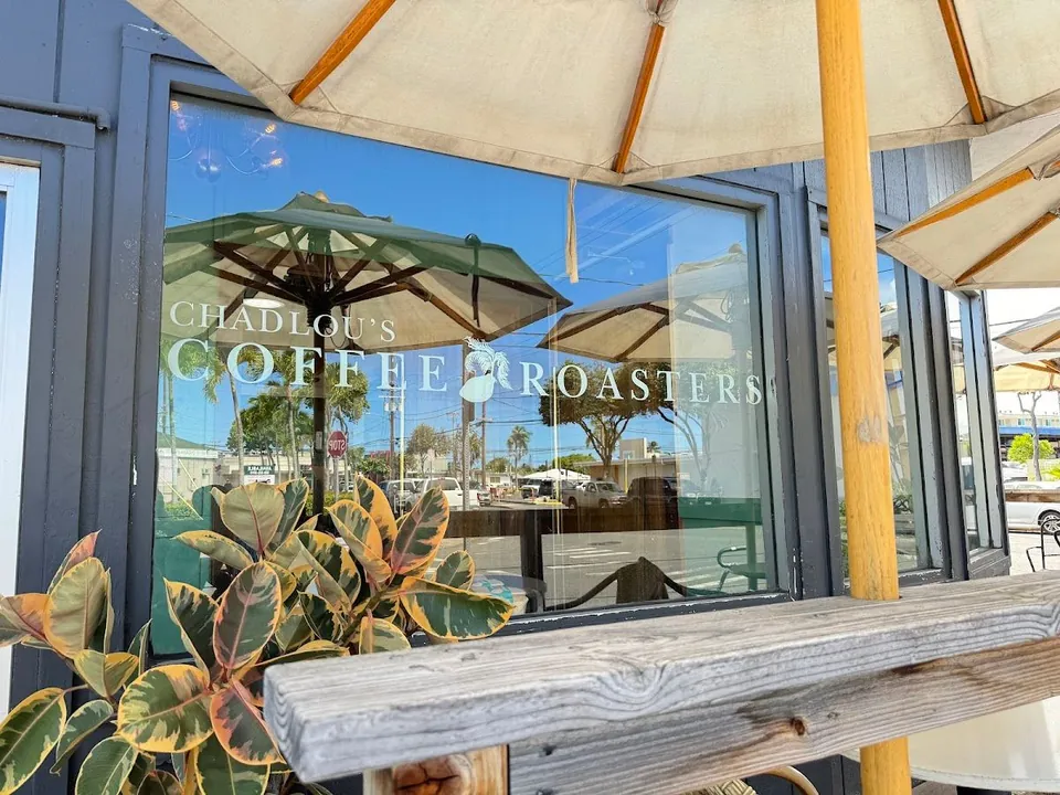 ChadLou's Coffee Roasters lettering on a dark storefront window, with patio umbrella, wood rail, and a leafy plant.