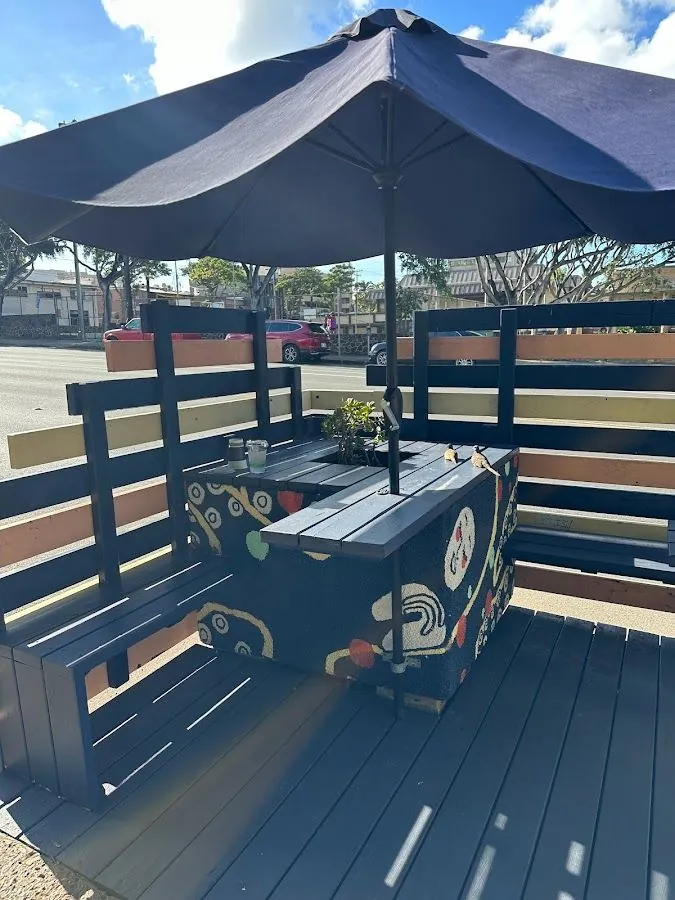 Shaded outdoor benches and a painted table with cups and a small lizard, facing a street.
