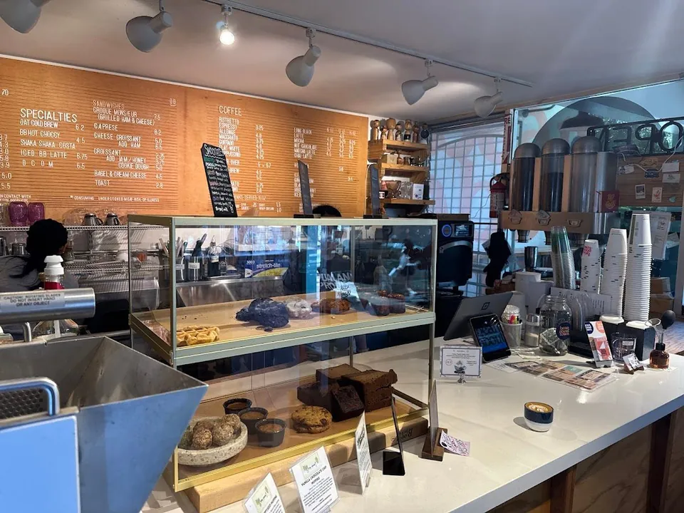 Coffee shop counter with a glass pastry case, espresso equipment, and a large wooden menu board on the wall.