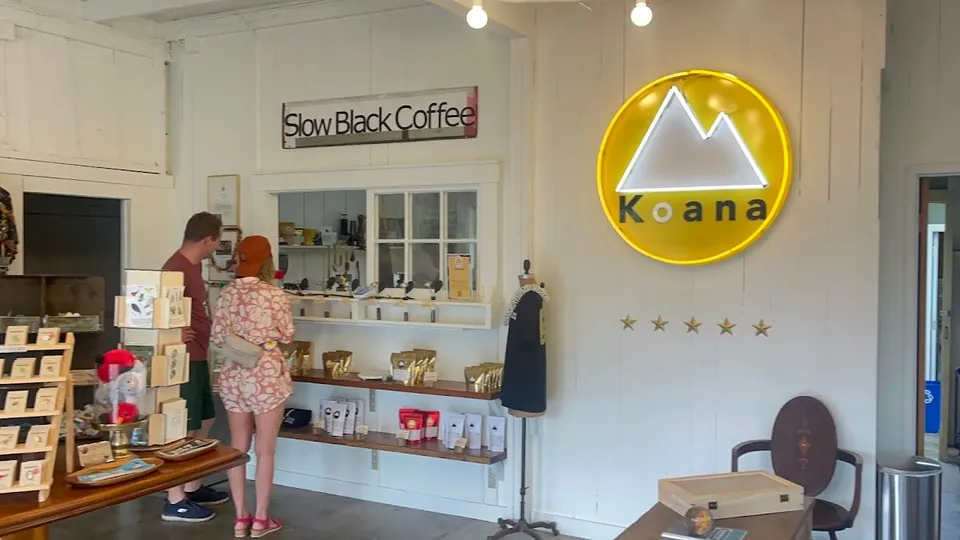 Two people look at shelves in a white shop interior with Slow Black Coffee and Koana signs.