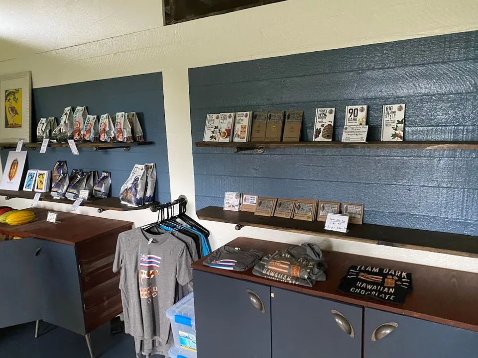 Retail shop interior with packaged bags, labeled chocolate bars, shirts, and blue cabinets.