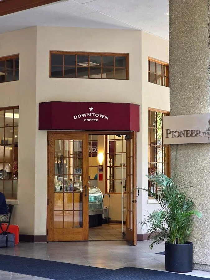 Shop entrance under a maroon Downtown Coffee awning, with open wooden doors and a potted plant.