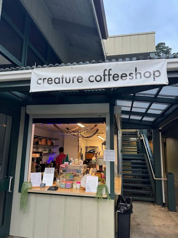 Service window and stairs at the creature coffeeshop storefront, with a person in a red shirt working inside.
