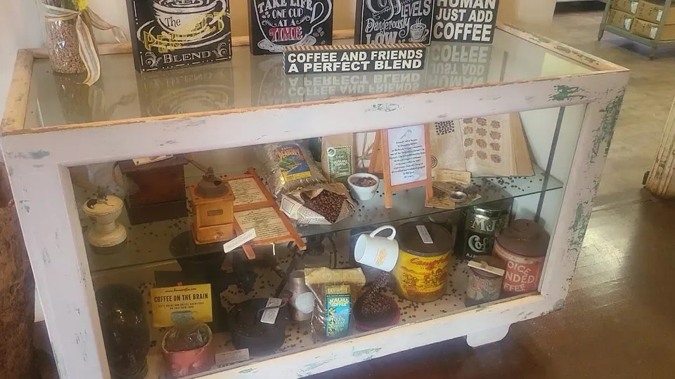 Glass display case holding coffee grinders, bean bags, tins, a mug, and coffee slogan signs.