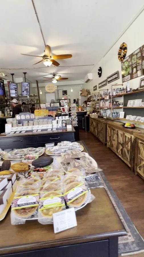 Cafe interior with wrapped pies on a front table, retail shelves along the wall, and staff behind the order counter.