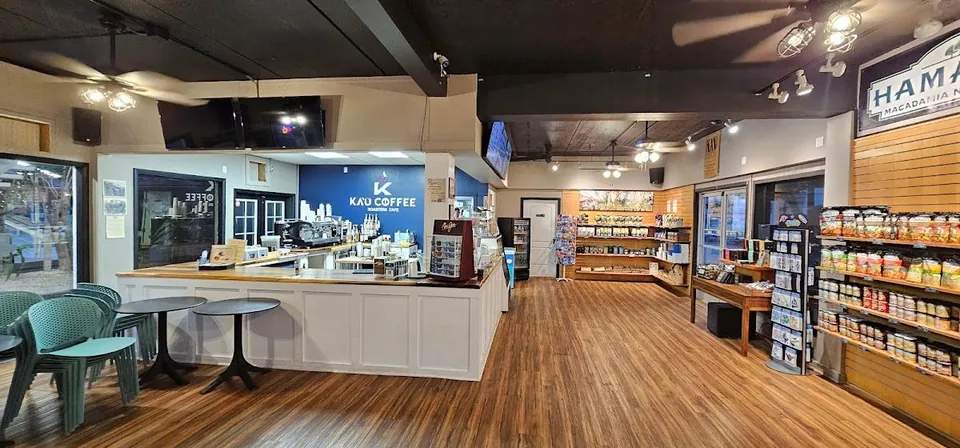 Coffee shop interior with a white service counter, cafe tables, and packaged-goods shelves.