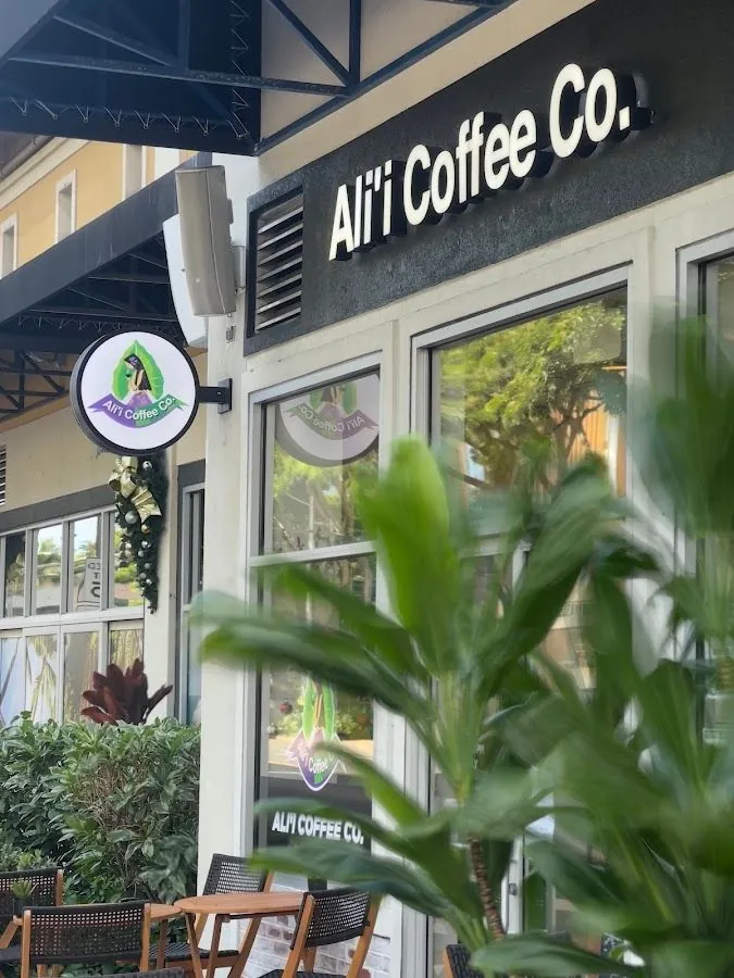 Storefront of Ali'i Coffee Co. with large white sign letters, a round hanging sign, and outdoor tables.