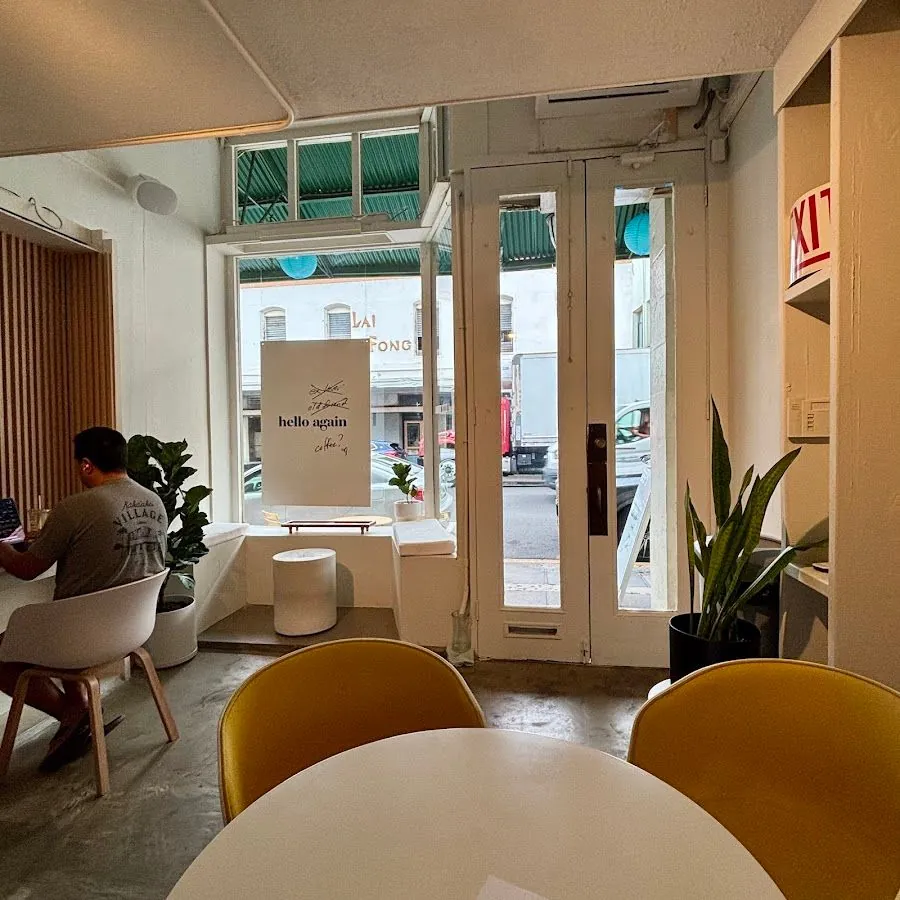 Cafe interior with yellow chairs, a white table, plants, and a person seated by the window.
