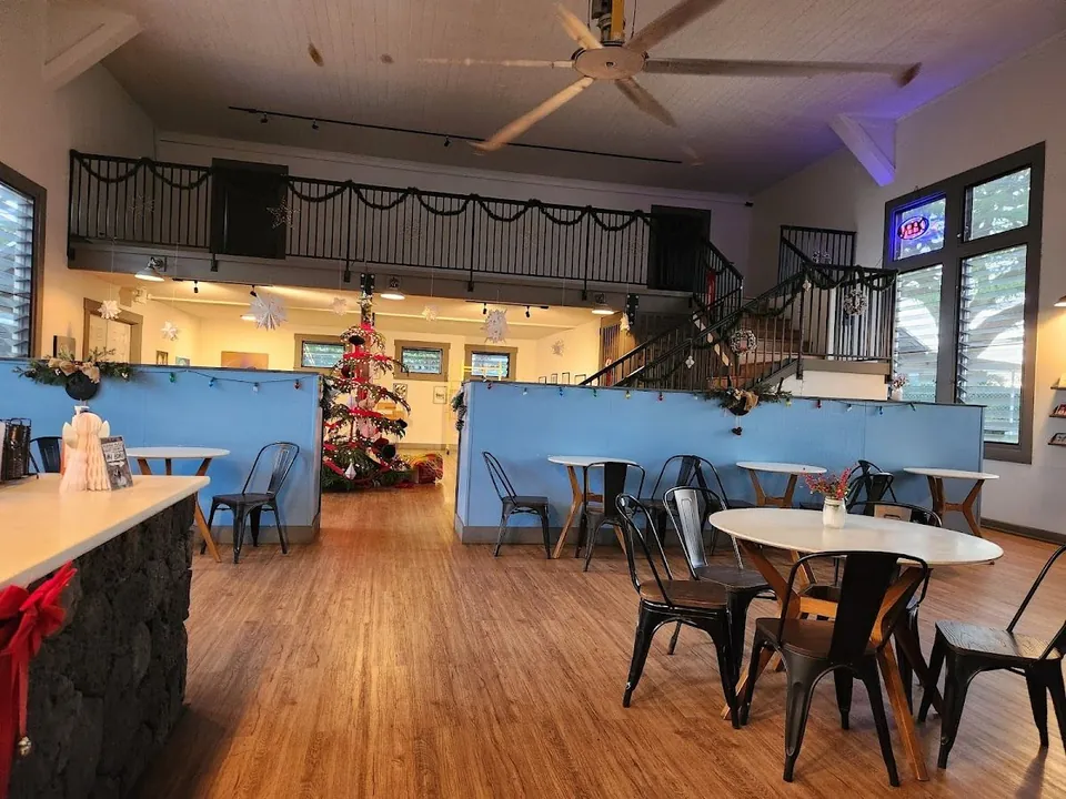 Holiday-decorated cafe seating room with blue partitions, round tables, metal chairs, a Christmas tree, and a loft.