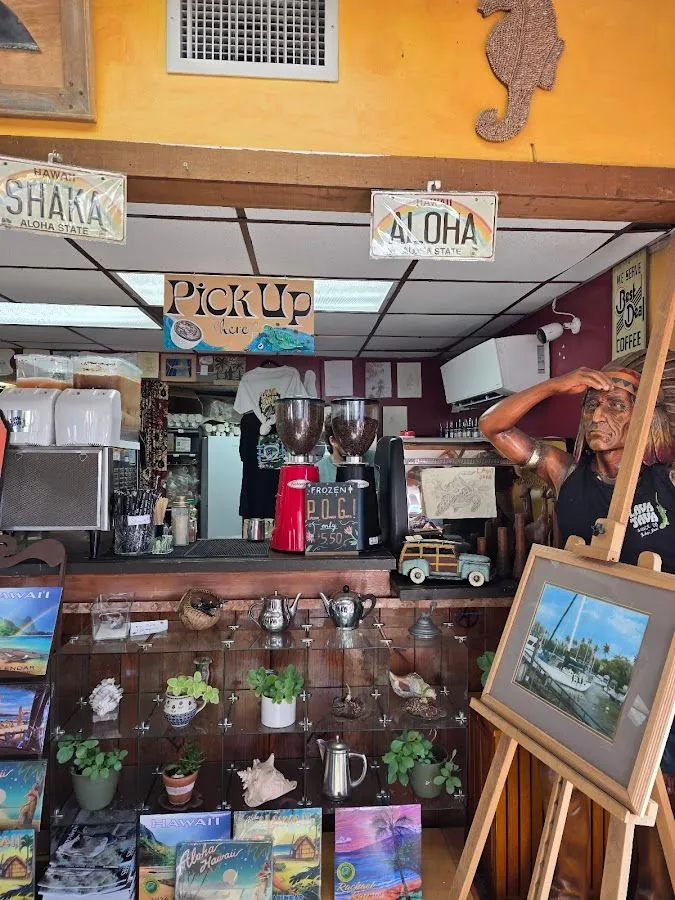 Shop interior with coffee grinders, a pickup sign, Hawaii plates, souvenir shelves, and a wooden figure.