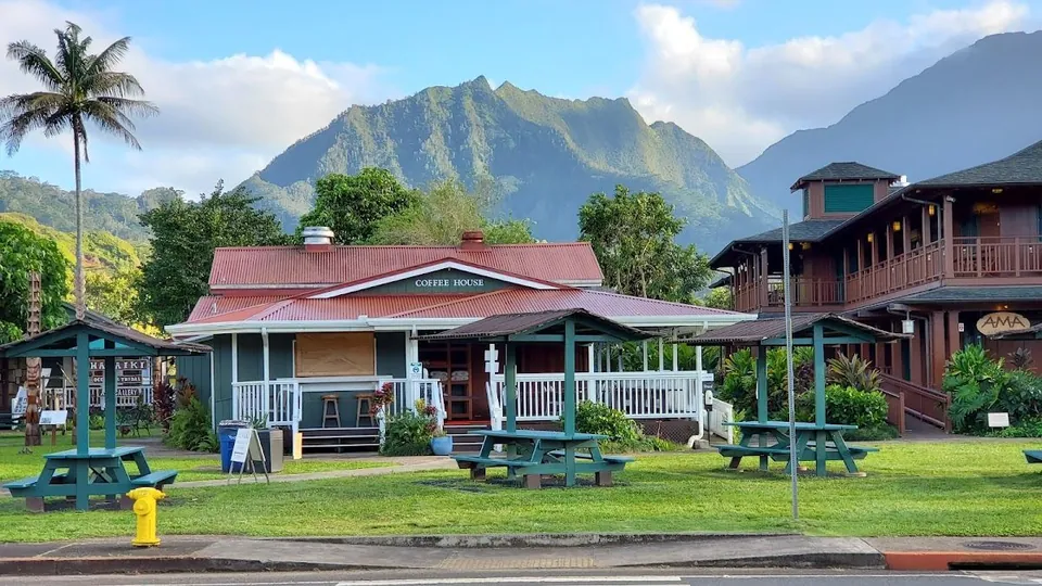 Green Coffee House with a red roof, picnic tables on the lawn, and mountains behind.