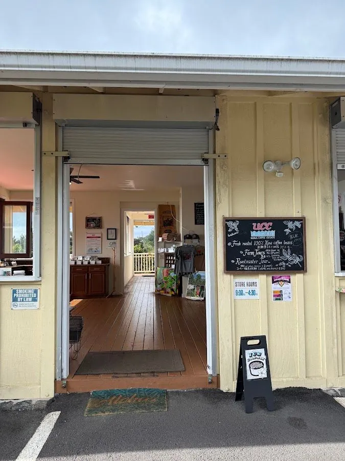 Open entrance of a pale yellow wooden building with a UCC coffee chalkboard and a store-hours sign.