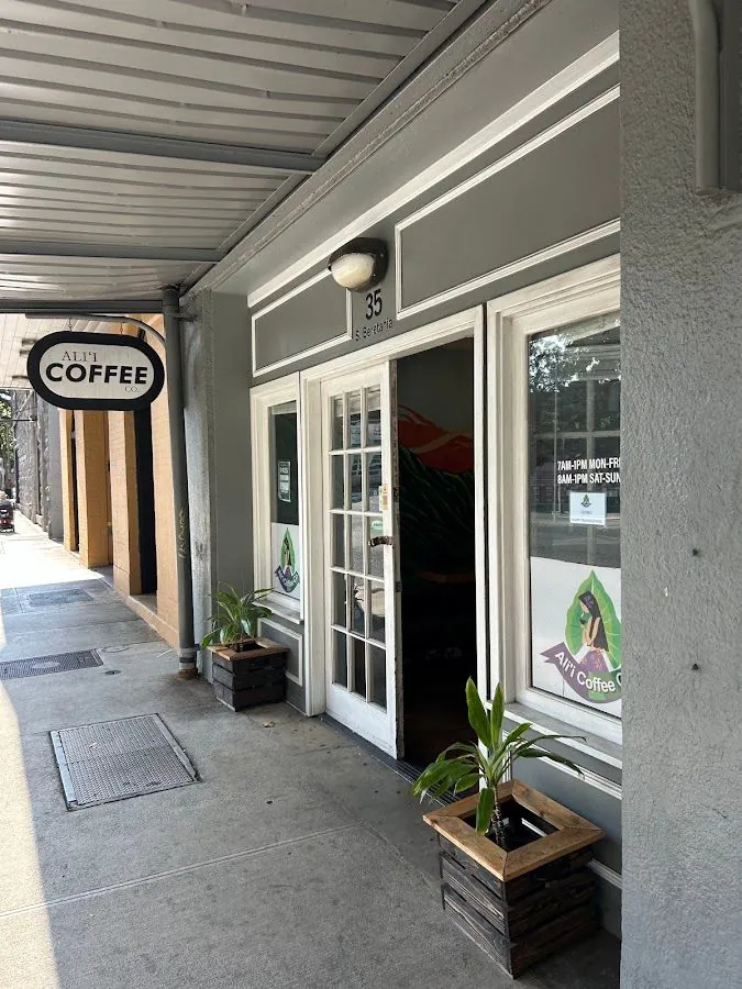 Covered sidewalk storefront of Ali'i Coffee Co. at 35 S. Beretania, with an open door, window hours, and crate planters.