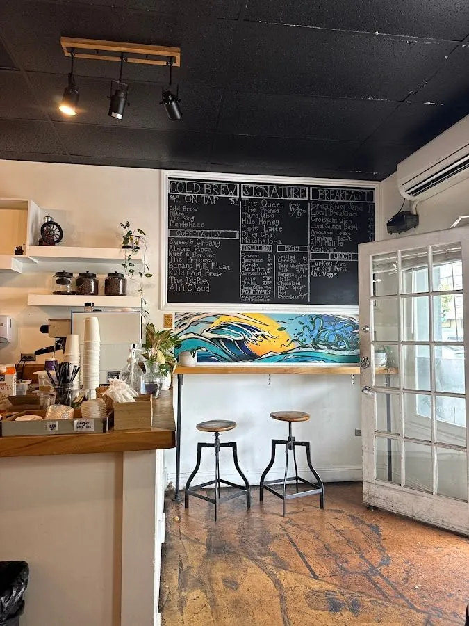 Cafe interior with a chalkboard menu, counter, two stools, and a wave mural.