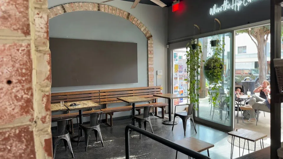 Cafe interior with bench seating under a brick arch and people seated at tables outside the window.